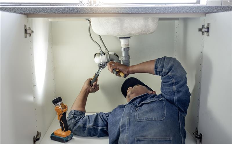 Plumber repairing pipes beneath a bathroom sink in Baldwin Park